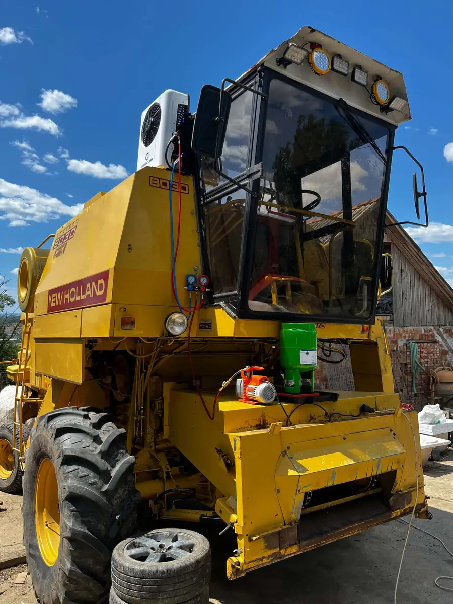 Combină New Holland 8030 galbenă, cu o unitate albă de climatizare în partea de sus, lângă cabină, și manometre racordate cu furtunuri roșu și albastru